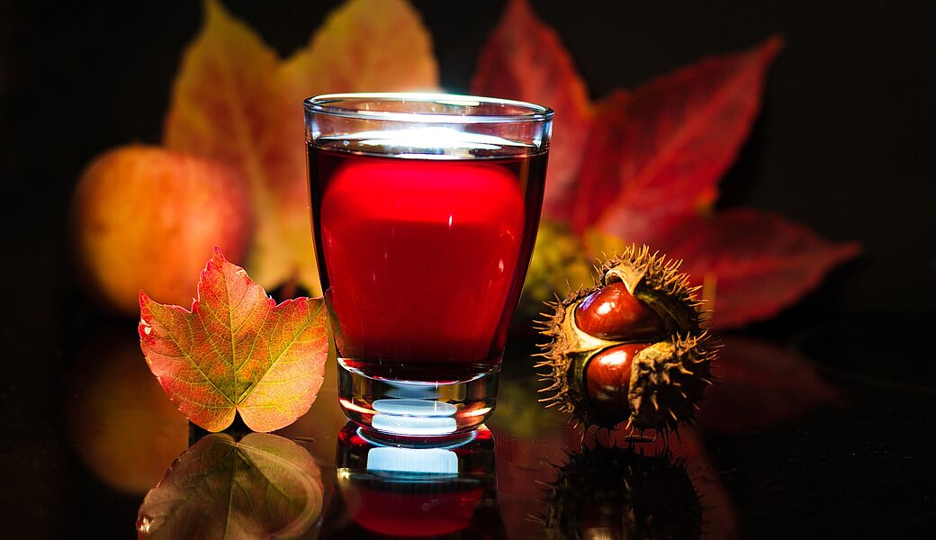 Glas Rostwein mit bunten Blättern und Kastanien