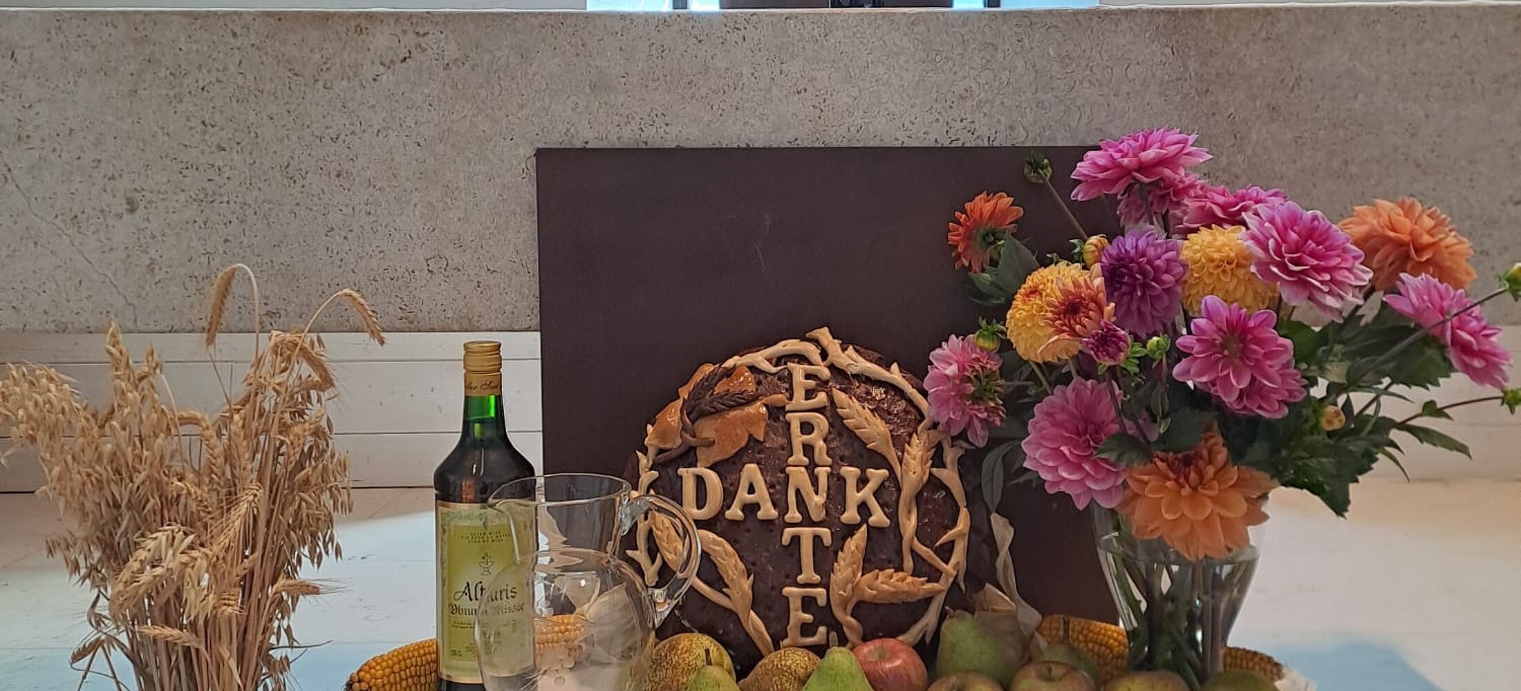 Brot, Wein, Getreide und Blumen vor einem Altar